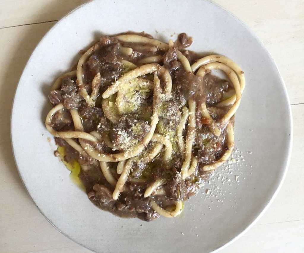 A close up of a white plate with long, thin pasta on it and a meat sauce and cheese