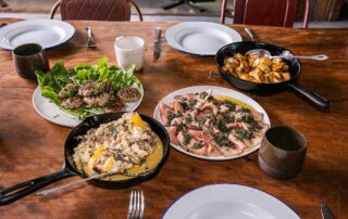 A dark wooden table with four dishes of food - meatballs, roast potatoes, rare beef and pork cooked in milk