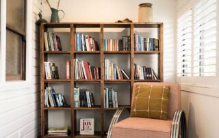 A cubed style wooden bookcase witjh a pink armchair in front of it at the Cromwell Farmhouse
