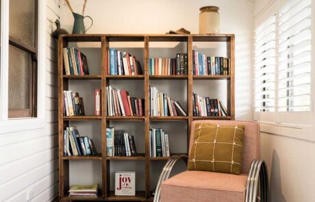 A cubed style wooden bookcase witjh a pink armchair in front of it at the Cromwell Farmhouse