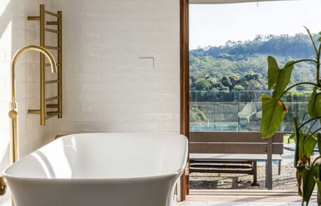 A white bathtub at the Cromwell Farmhouse with a green plant to the right and a view out of the open door to the pool area