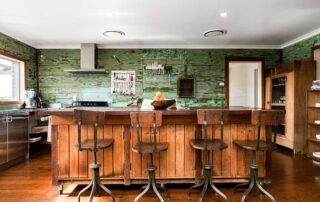 Large kitchen with green walls and a dark timber floor and island bench. Four wooden stools sit at the island bench.