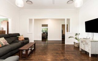 A large, spacious, white living room with tv, dark wooden floors and a black couch opposite the tv.