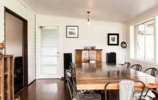 A white-walled dining room at the Cromwell Farmhouse with dark timber flooring and a large timber dining table and eight chairs