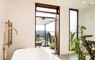 A white bathtub at the Cromwell Farmhouse with a green plant to the right and a view out of the open door to the pool area