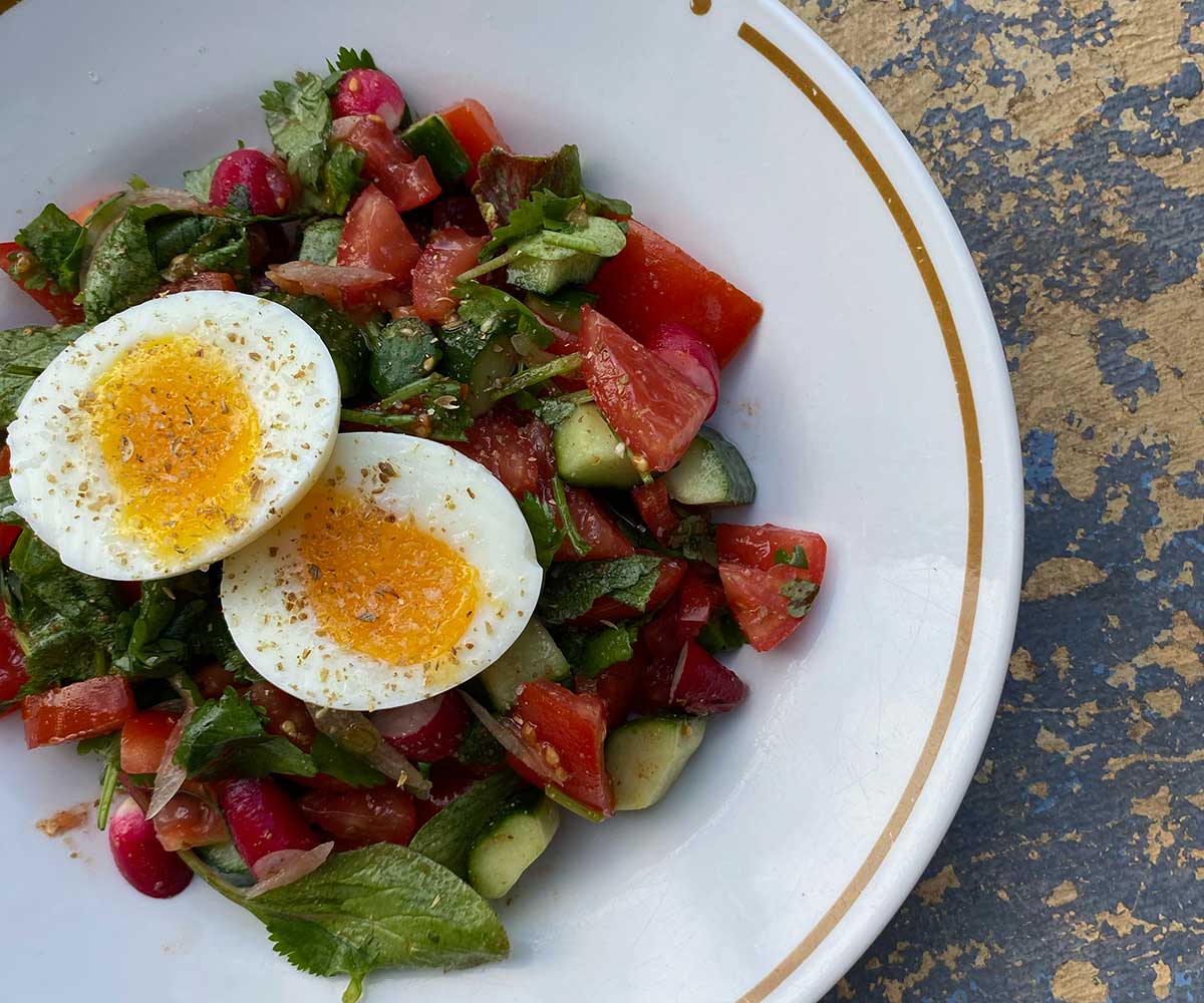 Kachumber salad of chopped tomatoes and cucumber on a white plate with a boiled egg