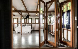 Middle Shed interior with polished concrete floors and wooden framed bi-fold glass doors to the bedroom with a queen bed with white bedding