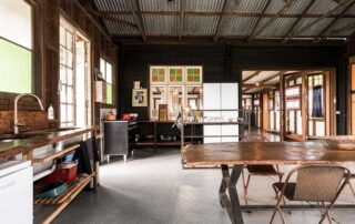 Middle Shed large open plan kitchen with a wooden top dining table, white double door fridge, open sink bench and interior windows