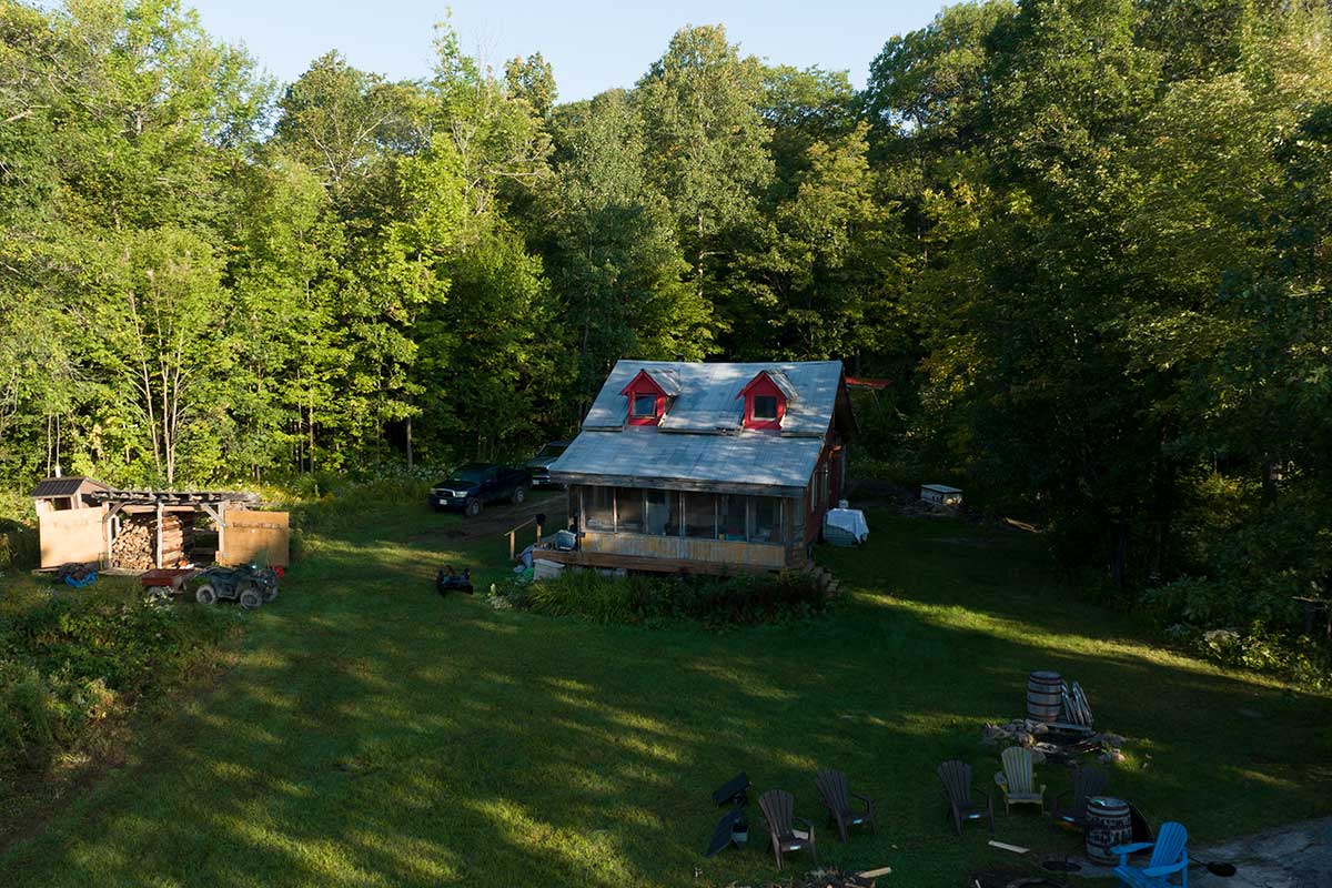 A cabin in the forest with cleared land at the front and trees behind