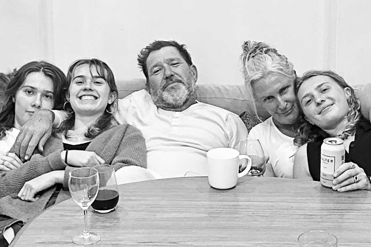 Grayscale image of a happy family of five sitting back on a couch with a table in front of them with drinks on it